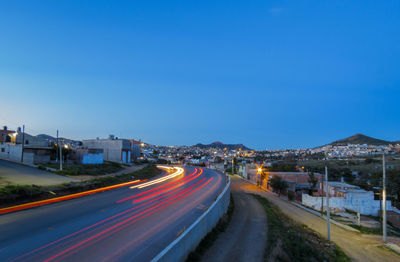 Light trails on road against blue sky at dusk