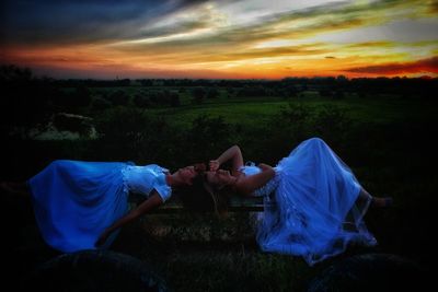 Women sitting on field against sky during sunset
