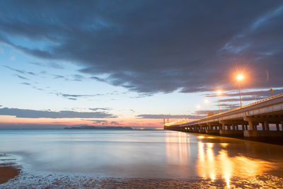 Illuminated bridge over sea against sky at night