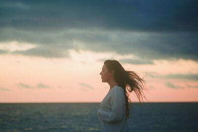 Side view of woman standing against sea during sunset
