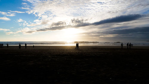 Silhouette people at beach against sky during sunset