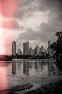 Modern buildings by river against sky in city