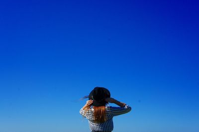 Rear view of woman wearing hat standing against clear blue sky during sunny day