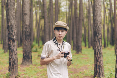 Portrait of man standing by tree trunk in forest