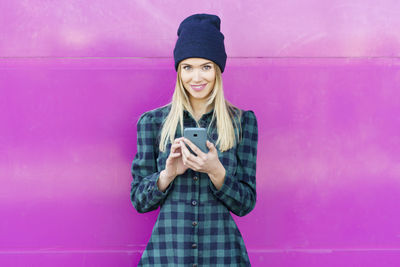 Portrait of smiling young woman standing against pink wall