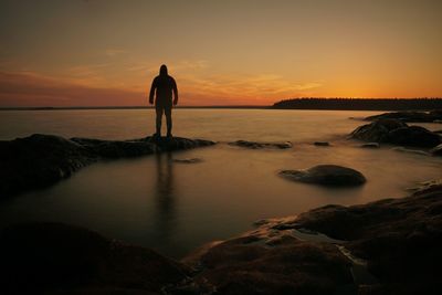 Silhouette woman standing on rock at sunset