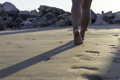 Low section of woman walking on sand at beach