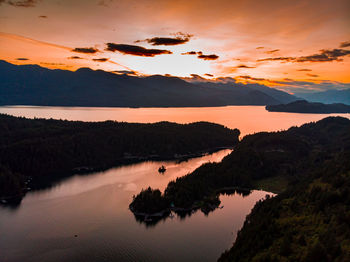 Scenic view of lake by silhouette mountains against orange sky