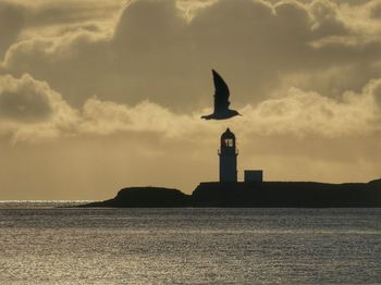 Silhouette of lighthouse on sea against sky