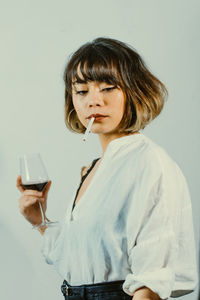 Woman smoking cigarette while having red wine against white background