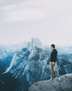 Rear view of man standing on rock against sky