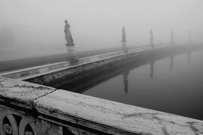 Sculptures over river at prato della valle during foggy weather