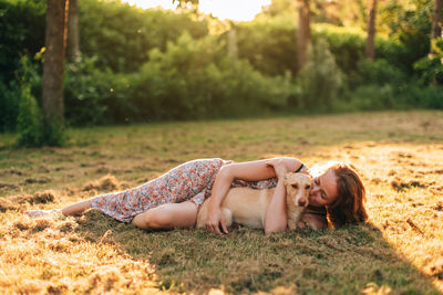 Woman lying on the grass embraces and cuddles her dog in the light of the sunset in a bucolic scene