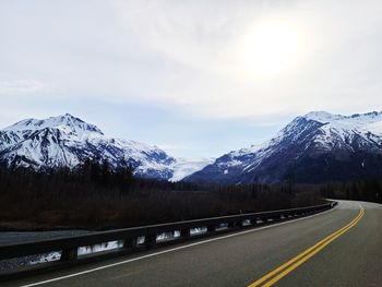 Road by snowcapped mountains against sky during winter