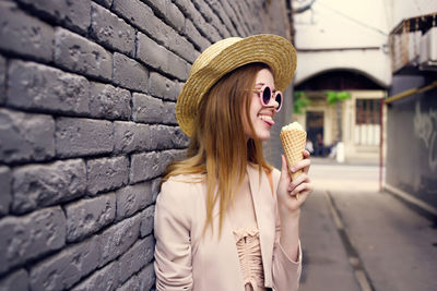 Young woman holding ice cream against brick wall