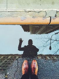 Reflection in puddle of man waving hand and photographing