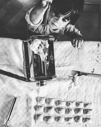 High angle view of boy holding pasta maker by ravioli on table