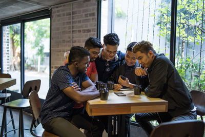 Friends using mobile phone while sitting in cafe