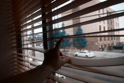 Cropped image of person touching blinds while looking through window