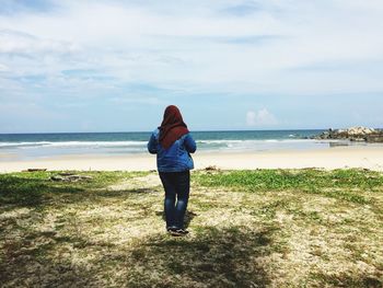 Rear view of woman standing on beach against sky