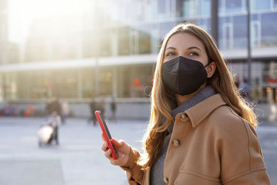 Attractive woman wearing black mask ffp2 kn95 holding smartphone outdoors