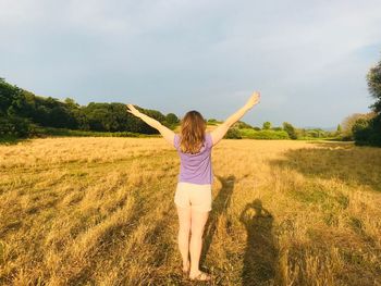 Rear view of woman with arms raised standing on field against sky