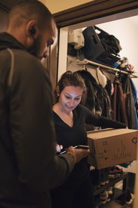 Mid adult woman using mobile phone to sign for her delivery from messenger at doorway