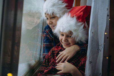 Cute brothers wearing santa hat embracing by window