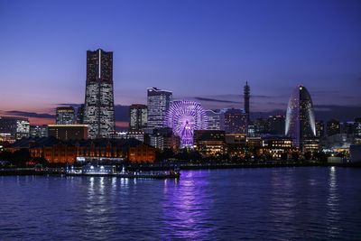 Illuminated city by river against sky at night