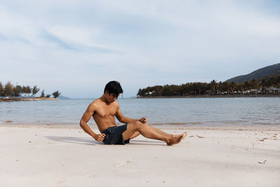 Rear view of woman sitting at beach against sky