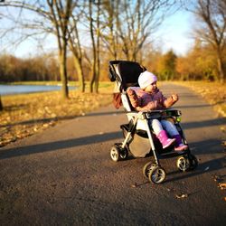 Cute toddler wearing warm clothing while sitting in baby stroller at park during autumn