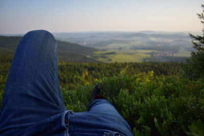 Low section of man relaxing against green landscape during sunset