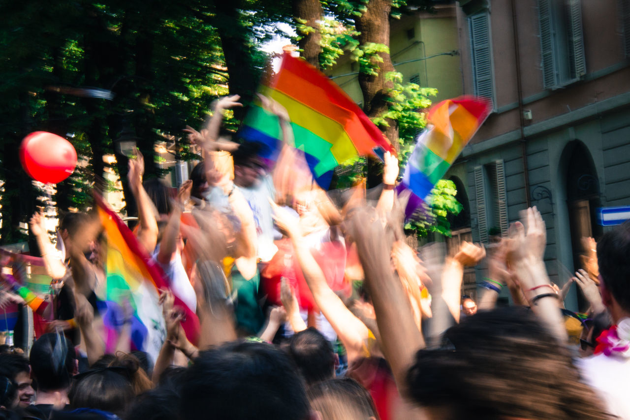 large group of people, multi colored, blurred motion, celebration, real people, motion, enjoyment, crowd, women, fun, men, outdoors, architecture, day, building exterior, city, bubble wand, adult, people