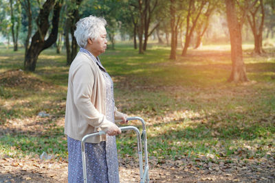 Side view of senior man holding umbrella standing against trees