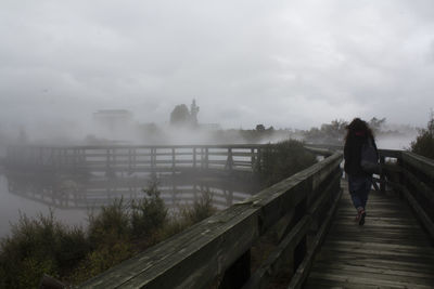 Rear view of woman walking on footbridge on foggy day