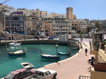 Boats moored in canal by buildings in city against sky