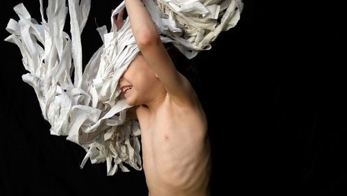 Shirtless boy playing with white fabric against black background