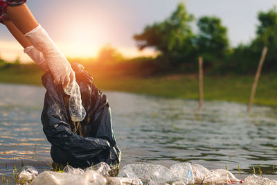 Man holding umbrella by river against sky during sunset