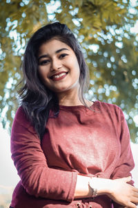 Portrait of smiling young woman standing against trees