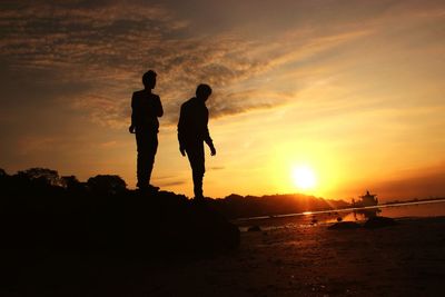 Silhouette people standing on beach during sunset