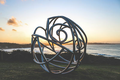 Metallic structure on beach against sky during sunset