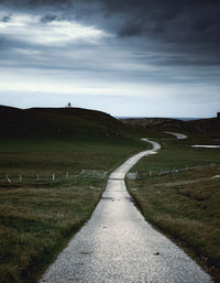 Empty road amidst field against sky