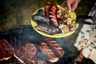 Close-up of hand holding meat on barbecue grill