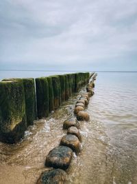 Wooden posts in sea against sky