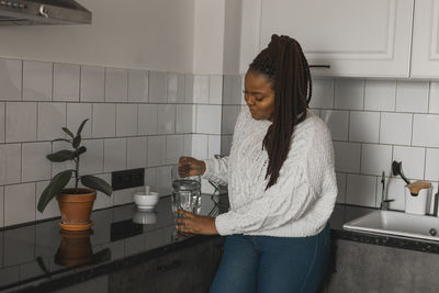 Side view of young woman drinking water at home