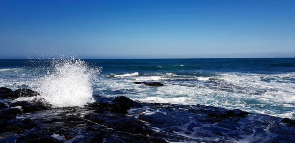 Waves splashing on sea against clear blue sky