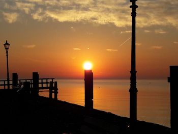 Silhouette wooden posts on beach against sky during sunset