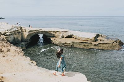 High angle view of woman standing on cliff at beach against sky