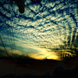 Low angle view of electricity pylon against cloudy sky