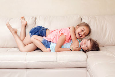 Side view of happy sisters embracing while lying on sofa